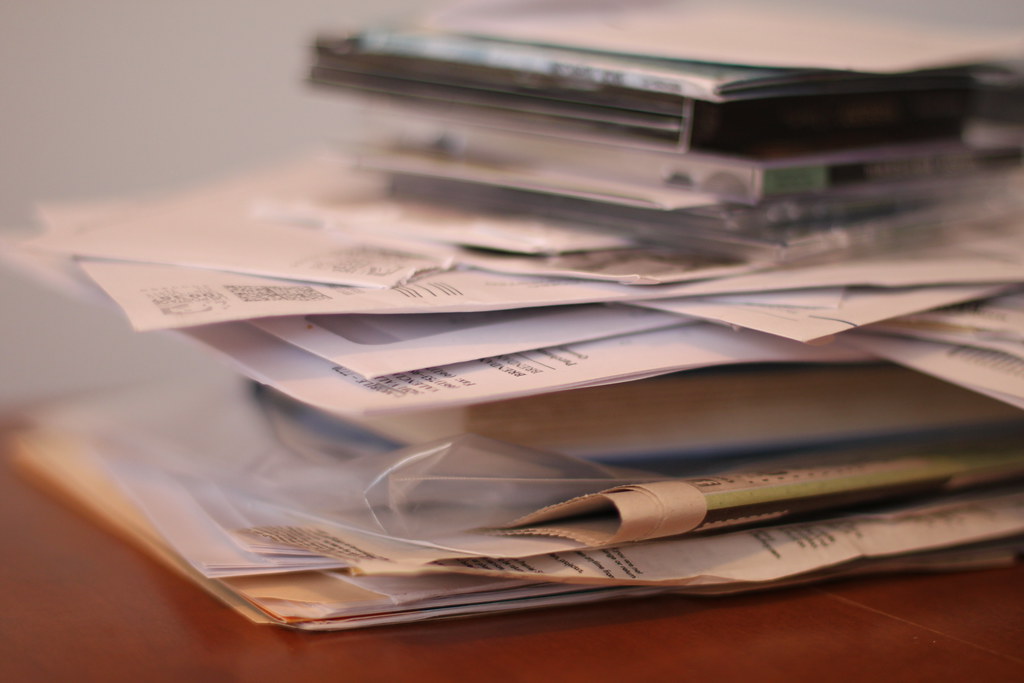 A thick pile of printed reports and paperwork stacked on an office desk, representing an unresolved vulnerability remediation backlog