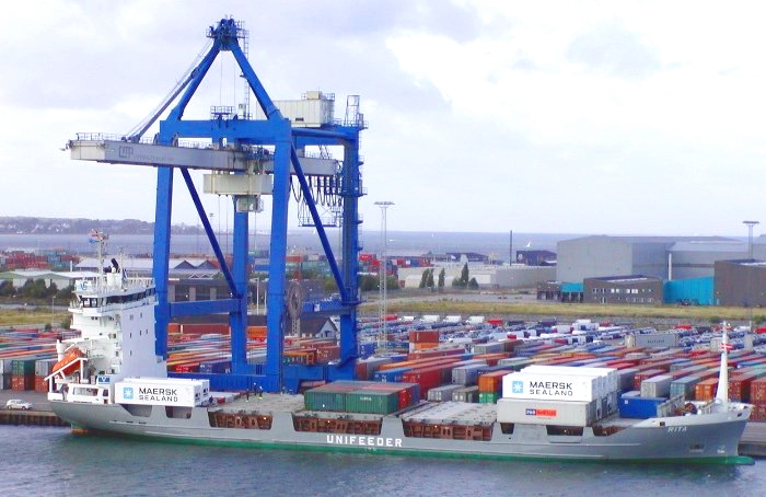 A container ship being loaded, with gantry cranes and stacked containers on the quay